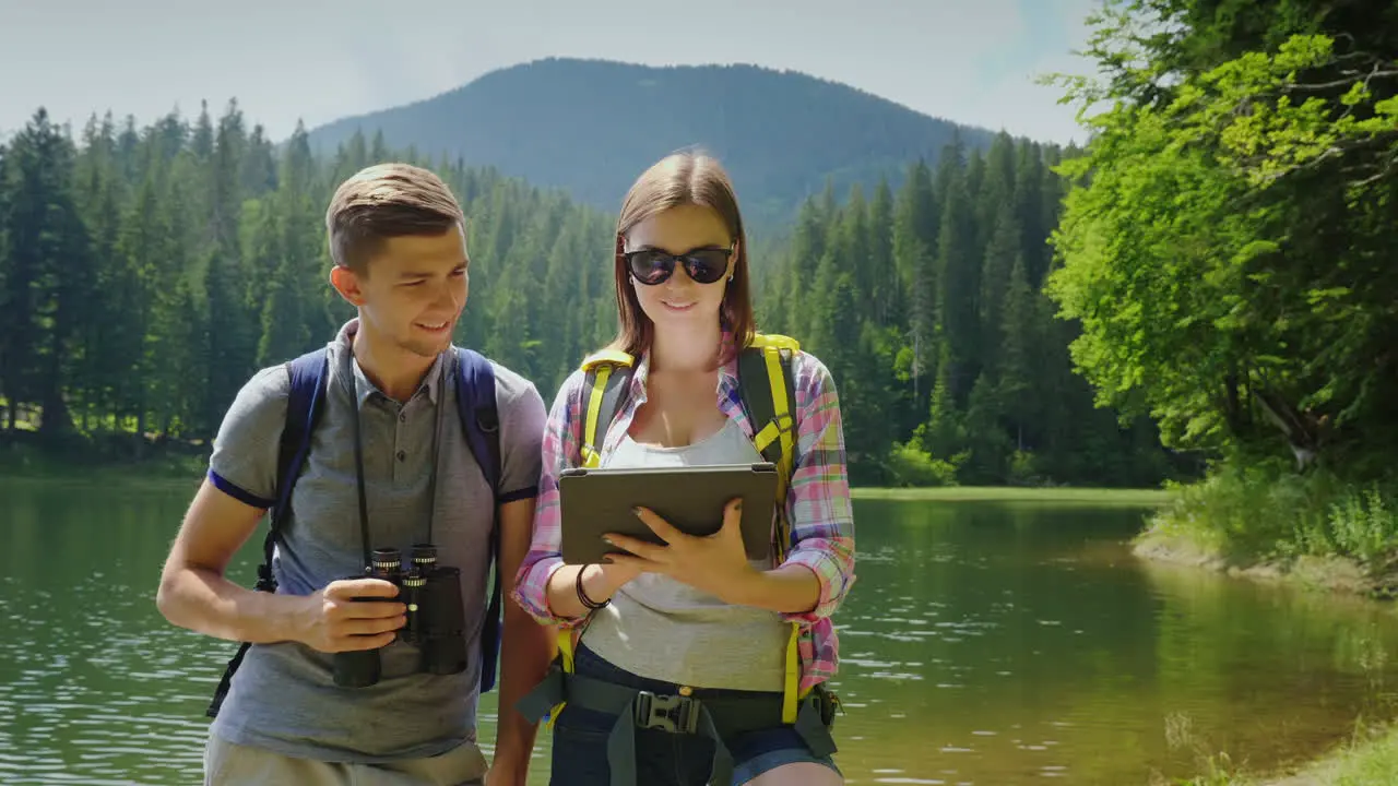 Man And Woman Travelers Together They Orient Themselves On The Map The Man Looks Through Binoculars 