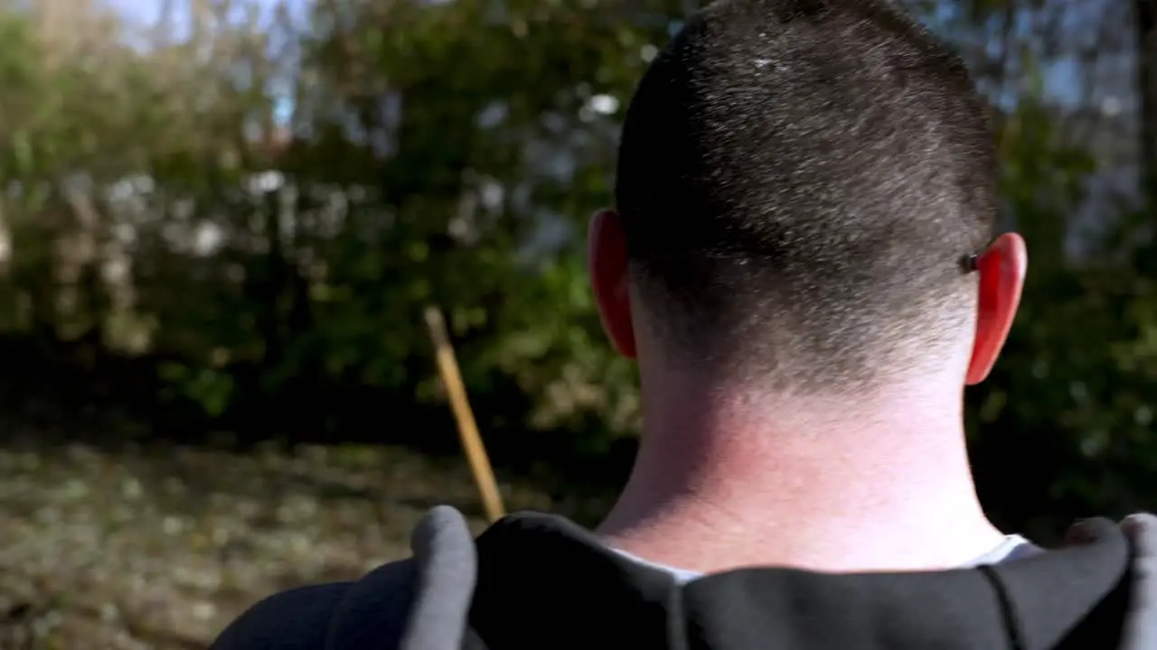 Adult man wearing sunglasses smoking a cigarette in backyard Orbiting shot from behind