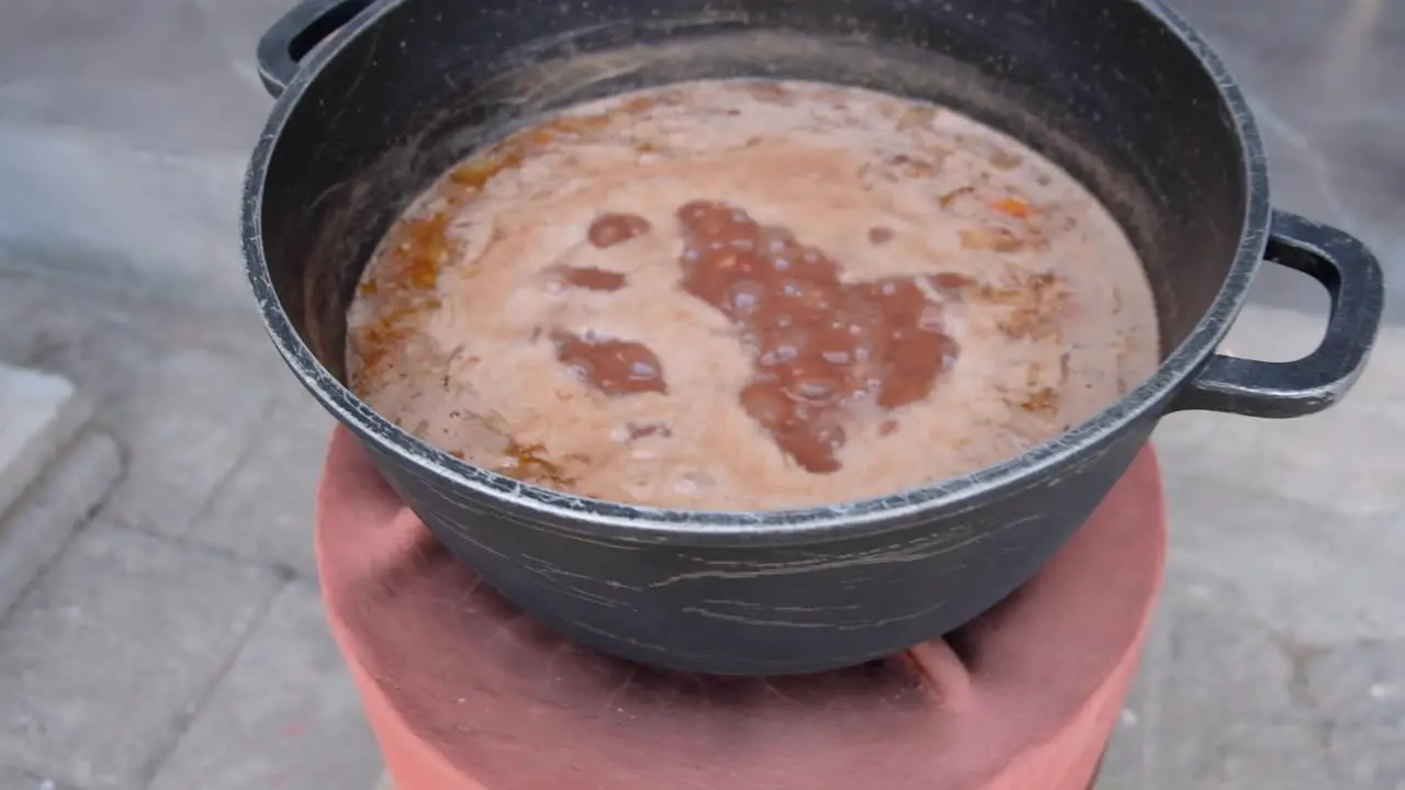 Flames burning kindling wood inside a clay cook stove and large pot of stew cooking on top