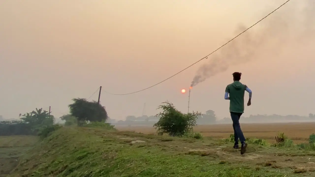 Slow motion shot of man jogging on rural path near Industry smokestack