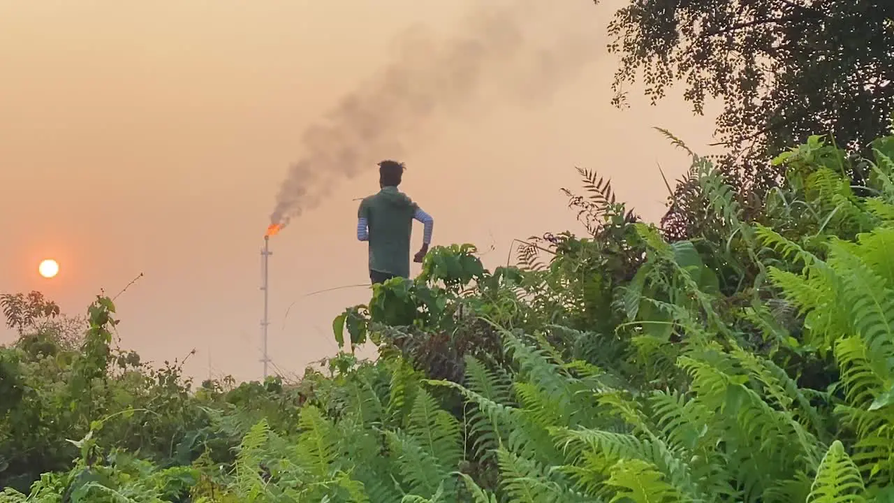 Jogger running by industrial area Gas Plant smokestack in sky tracking shot