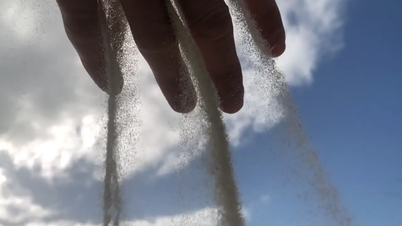 Slow motion of grains of sand falling in a waterfall concept from a hand with a blue sky background symbol of the time passing by