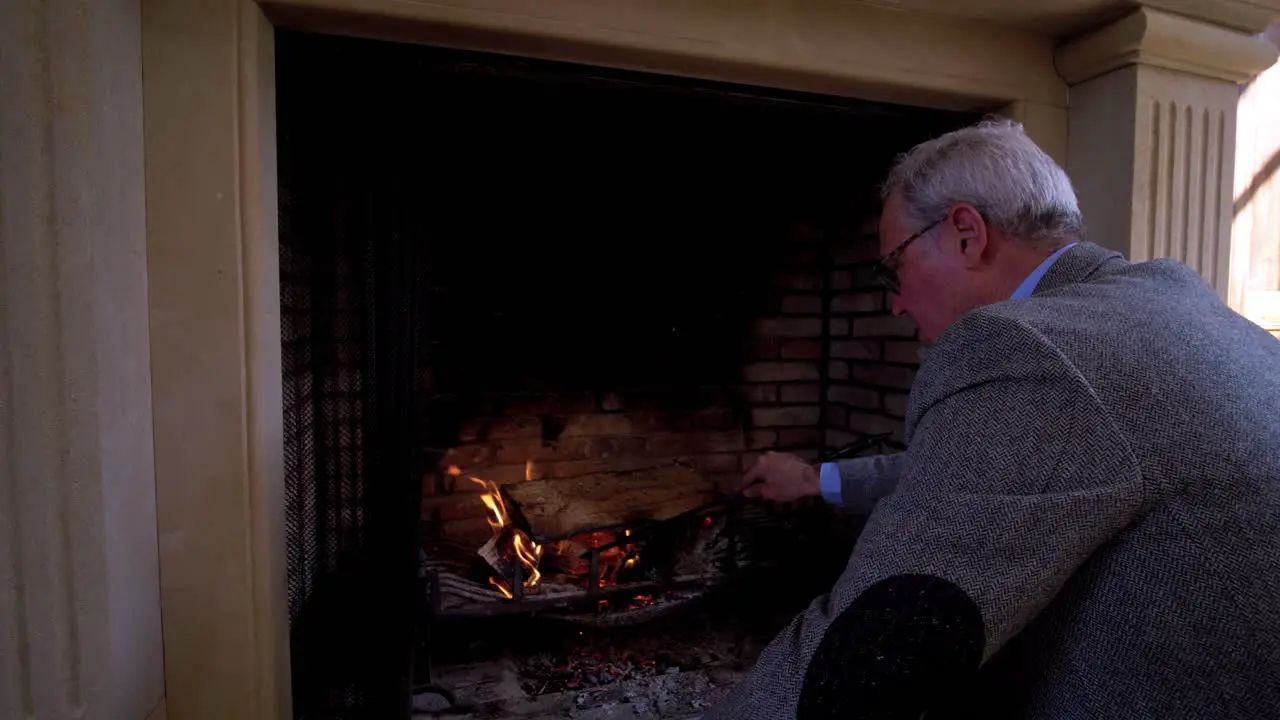 Slow motion shot of a senior man using a poker to move around wood in a fireplace