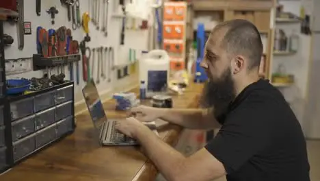 Caucasian master using laptop in bicycle workshop choosing part of bike online