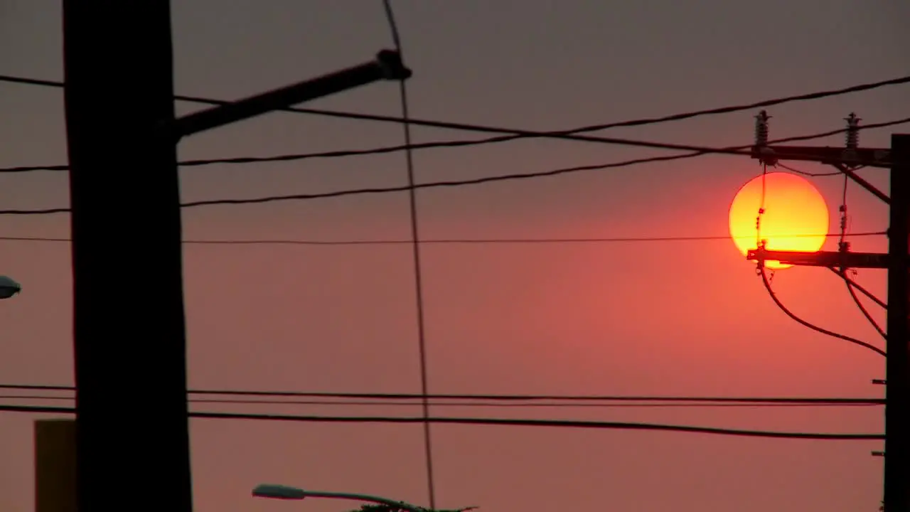 A orange ball of sun sets behind power lines during fire season in California