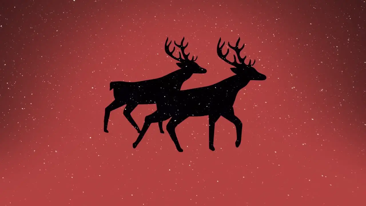 Snow falling over silhouette of two reindeers walking against orange background