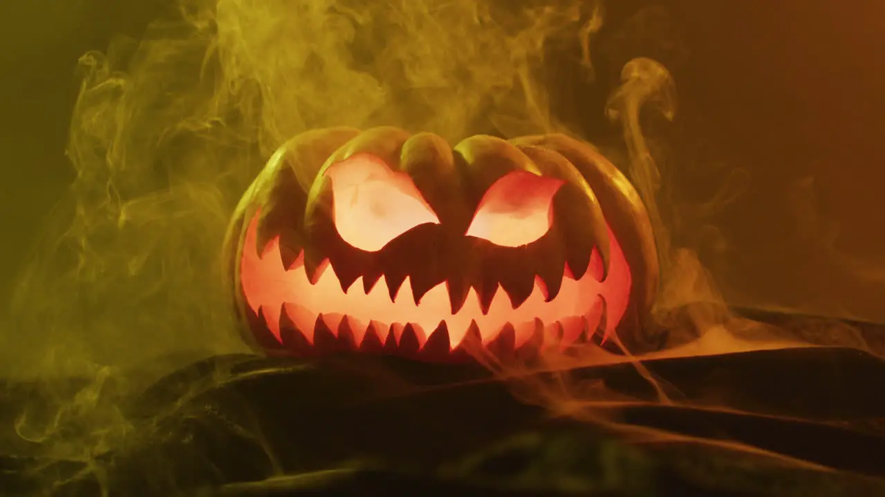 Video of halloween carved pumpkin with smoke and orange light on black background