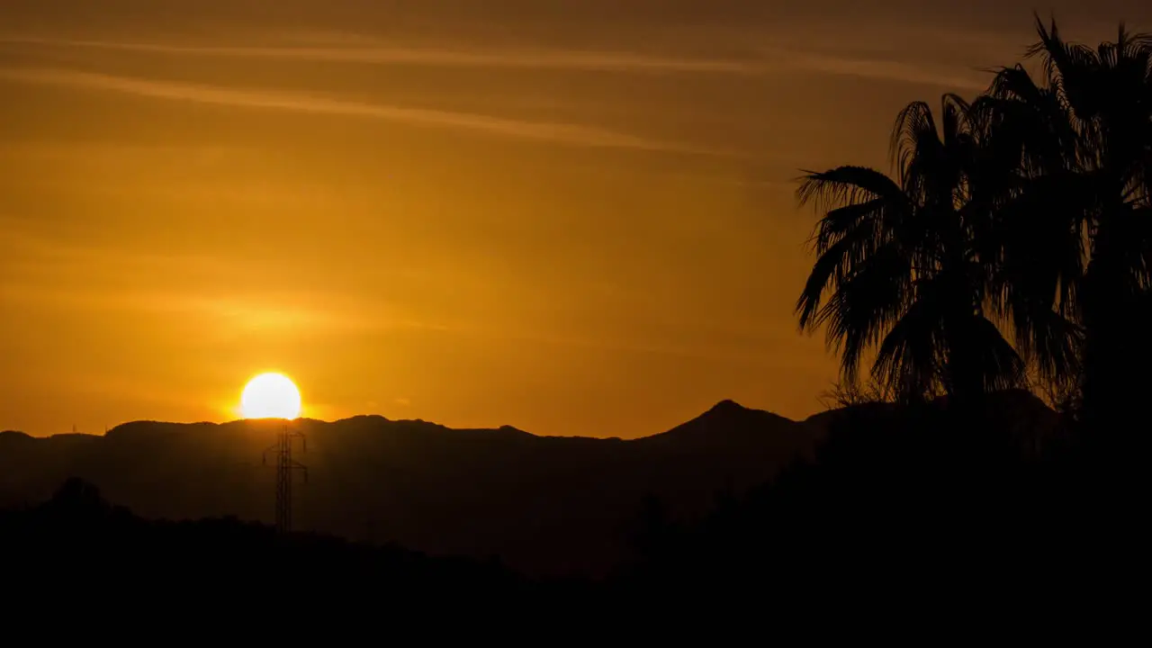 Beautiful 4k sunset time lapse filmed with zoom lens with palm trees in foreground and sundown behind majestic mountains in Mallorca Spain