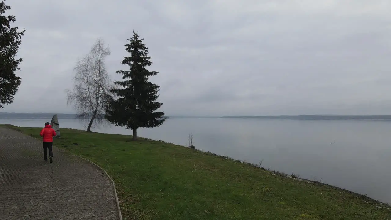 Man with orange jacket run next to the lake