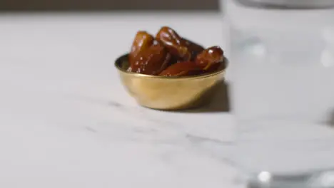 Close Up Of Bowl Of Dates And Glass Of Water On Marble Surface Celebrating Muslim Festival Of Eid