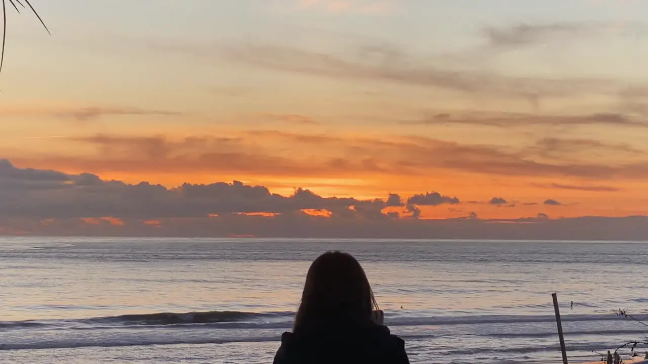 Silhouette of woman recording video over carcavelos beach and surfers at the sunset background on the Atlantic coast of Portugal