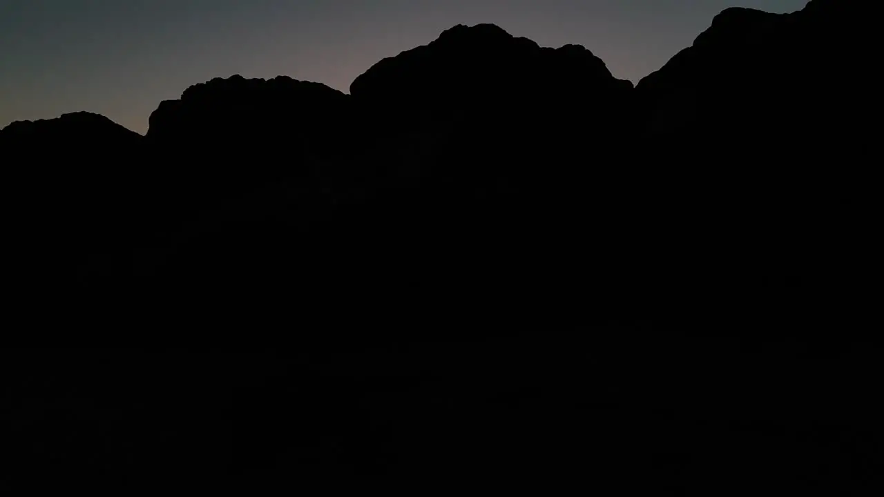 Slow shot rising above rocks and revealing sunset with silhouettes of people by the shore at San Buenaventura State Beach in Ventura California United States