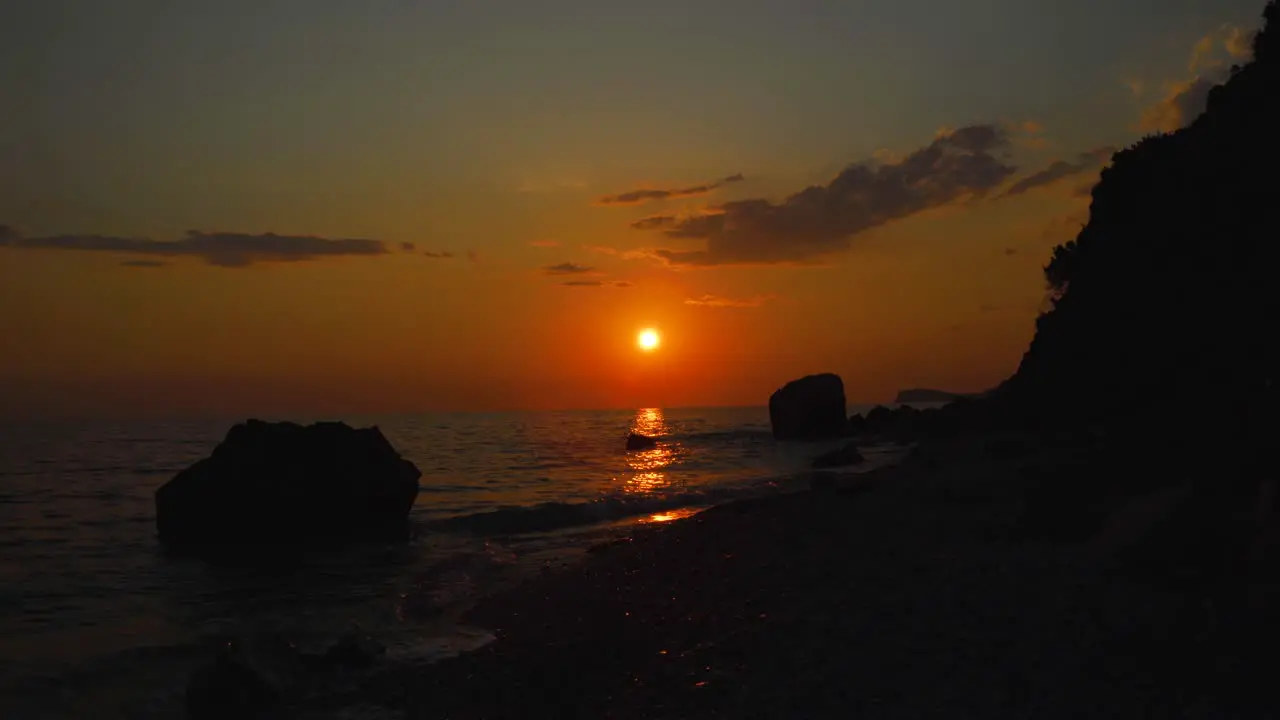 Seascape with rocky beach washed by sea reflecting beautiful sunset with orange cloudy sky