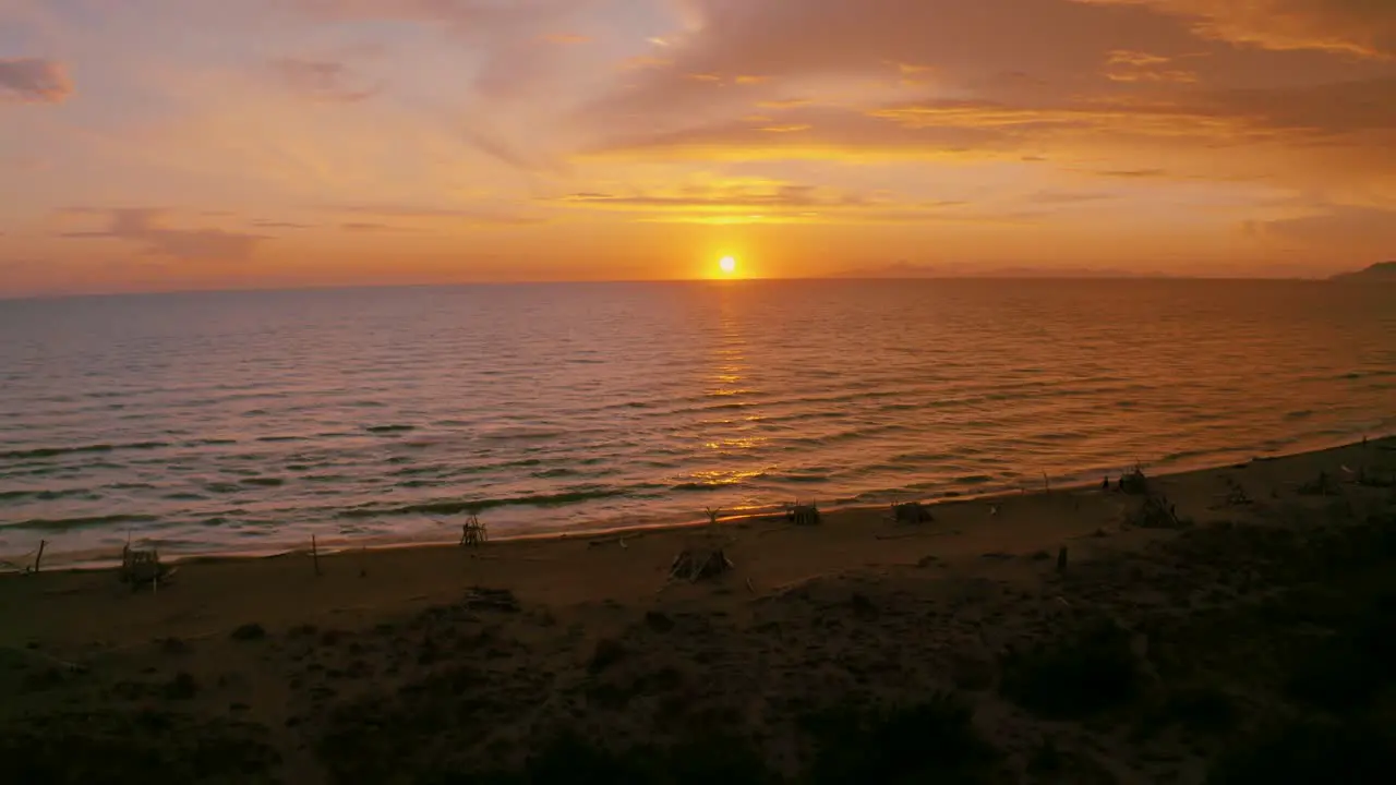 Aerial footage of the sunset at a sandy beach at the seaside in the iconic Maremma nature park in Tuscany Italy with a dramatic thunderstorm cloud sky and wooden tipis along the empty beach