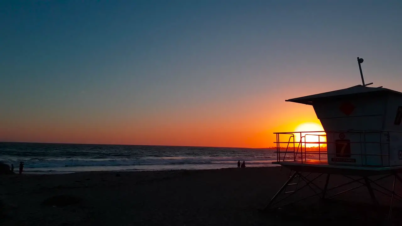 Slow sideways rising up sunset shot of Lifeguard house  tower with silhouettes of people by the shore at San Buenaventura State Beach in Ventura California United States