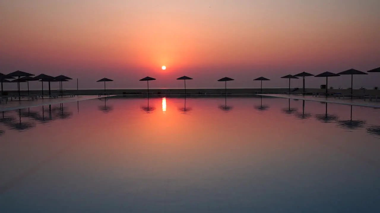 Perfect red sunset view from tropical hotel resort lounge with infinity pool beach umbrellas and their reflection