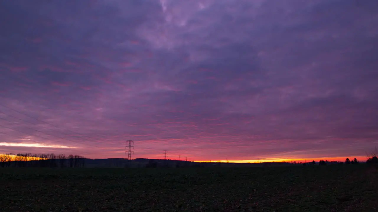 Landscape time lapse of electricity poles during a cloudy red purple sunset