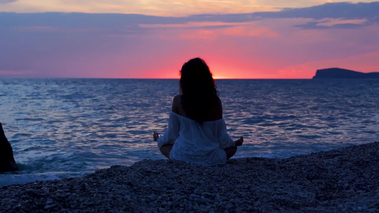 Yoga practicing on beautiful sunset with pink yellow sky reflecting over vibrant sea