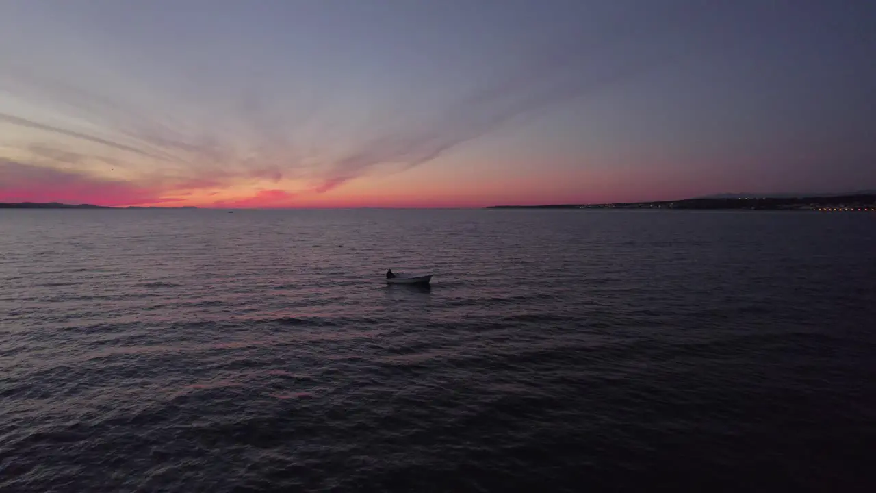 Small recreational fishing boat cruising on calm dark sea during twilight aerial