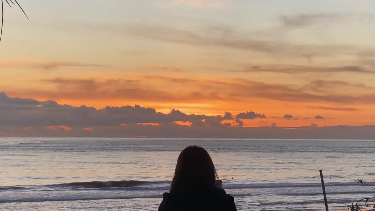 female tourist traveler on carcavelos beach takes photo of small waves breaking tourist woman standing in front of huge sunset over sea in the sunny day