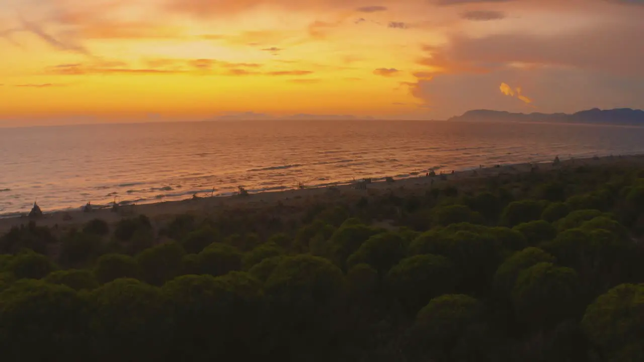 Aerial drone footage of the sunset at a sandy beach at the seaside in the iconic Maremma nature park in Tuscany Italy with a dramatic thunderstorm cloud sky and wooden tipis along the empty beach