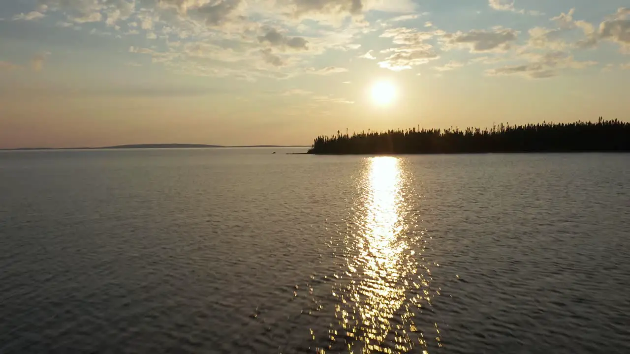 Drone moving towards a sunset over a lake and forest