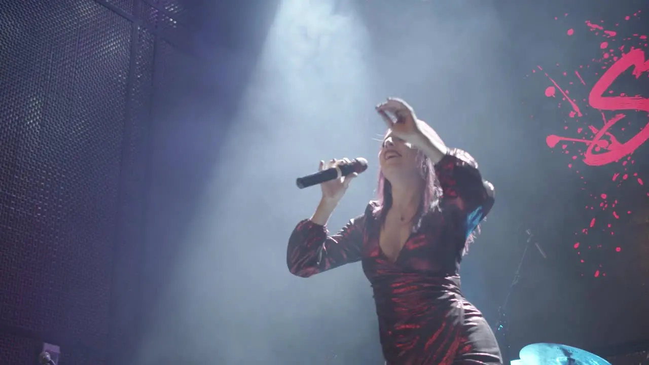 Young caucasian female singer performing and dancing by raising her arms on stage under a spotlight with a smoke machine effect