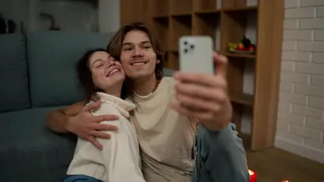 Lovely couple sitting on the floor together taking selfie with smartphone