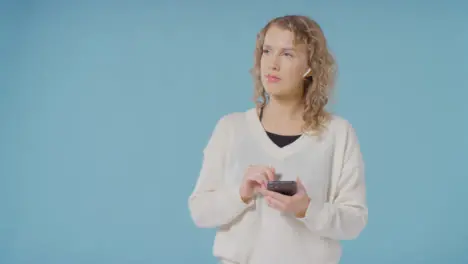 Studio Shot Of Young Woman Listening To Music On Mobile Phone And Dancing Against Blue Background 2