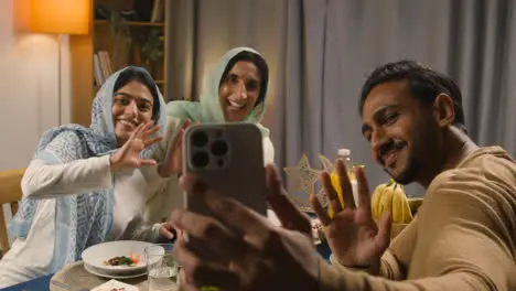 Muslim Family Making Video Call Sitting Around Table At Home Eating Iftar Meal Breaking Daily Fast During Ramadan