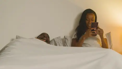 Couple At Home At Night Lying In Bed With Woman Looking At Mobile Phone 1