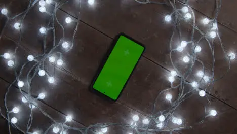 Overhead Shot Of Person Using Green Screen Mobile Phone Surrounded By Christmas Decorations And Lights