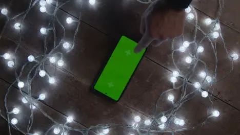 Overhead Shot Of Person Using Green Screen Mobile Phone Surrounded By Christmas Decorations And Lights 1