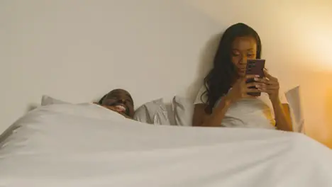 Couple At Home At Night Lying In Bed With Woman Looking At Mobile Phone 3