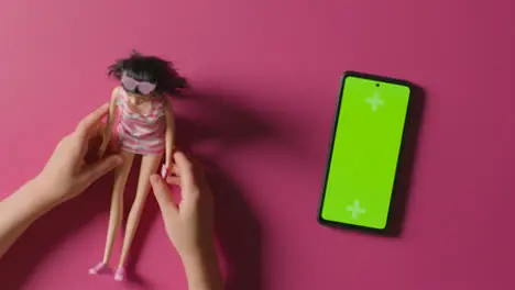 Overhead Shot Of Girl Playing With Toy Doll Next To Green Screen Mobile Phone