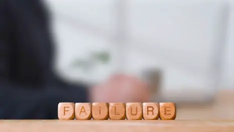 Business Concept Wooden Letter Cubes Or Dice Spelling Failure With Office Person Using Mobile Phone In Background