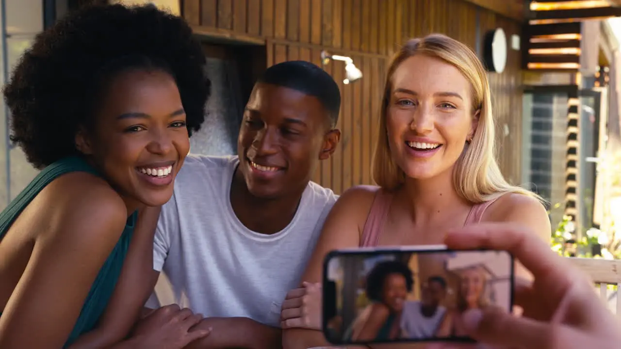 Group Of Smiling Multi-Cultural Friends Outdoors At Home Posing For Picture On Mobile Phone Together