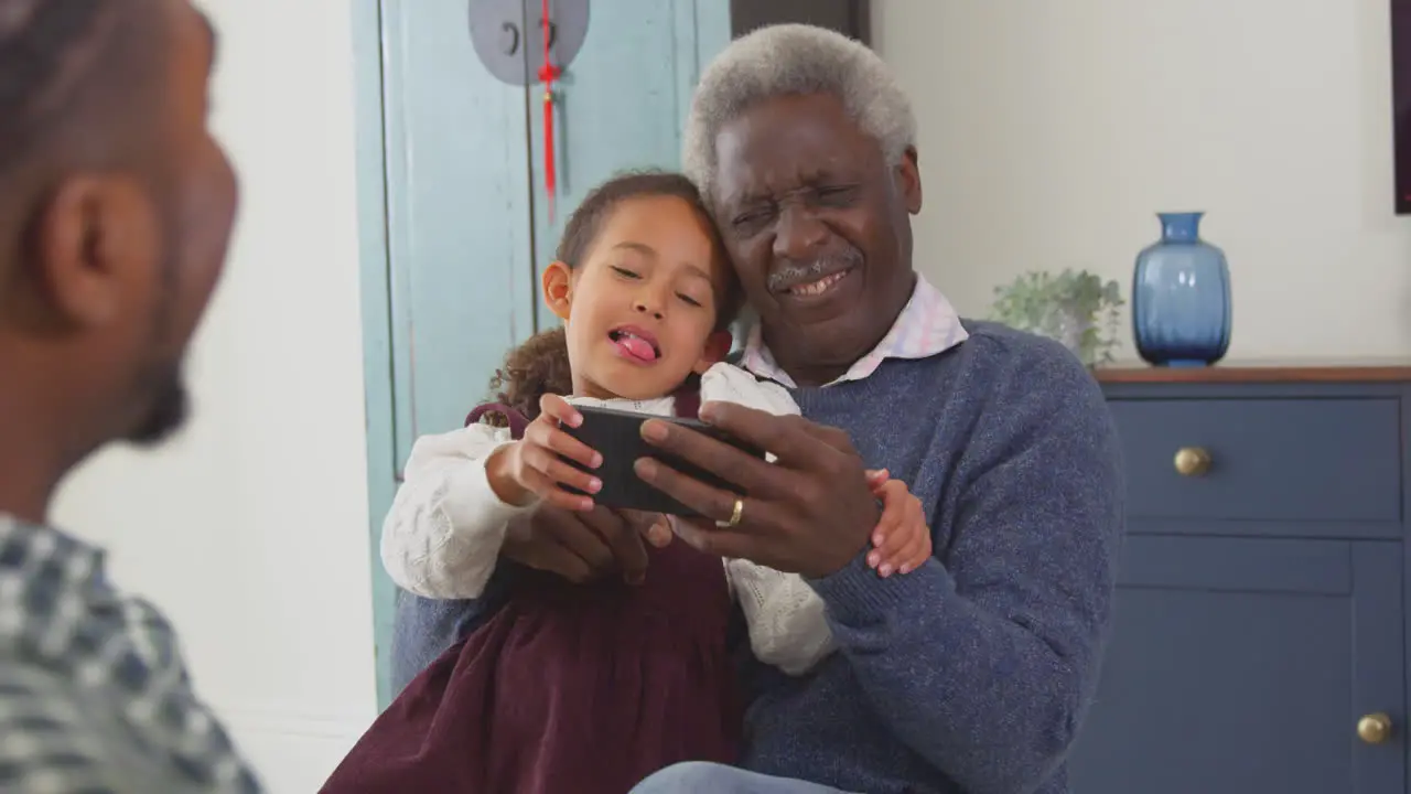 Grandfather with grandchildren playing game on mobile phone at home shot in slow motion