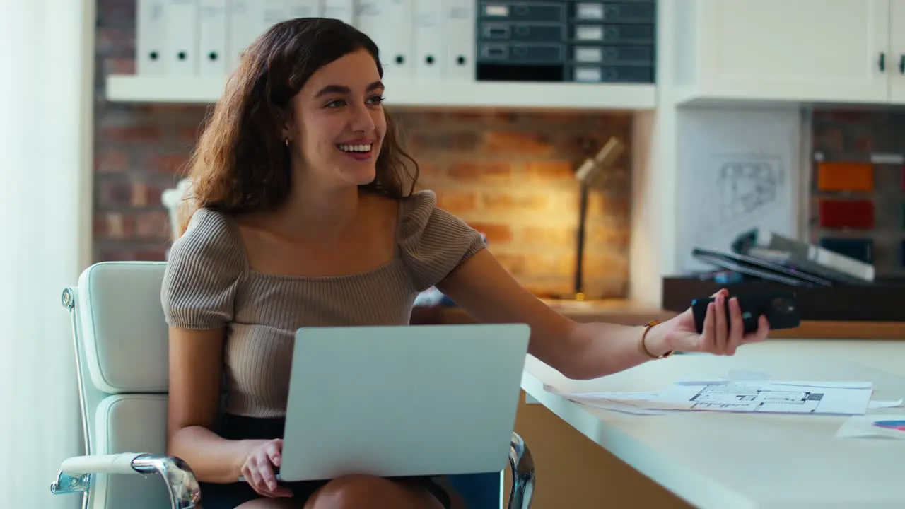 Young Smiling Businesswoman Working On Laptop At Desk In Office Talking On Mobile Phone