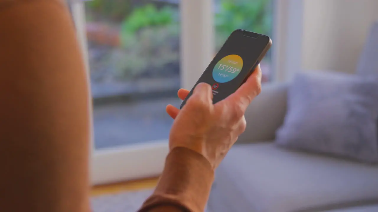 Close Up Of Man At Home Looking At App On Smart Phone To Control Heating