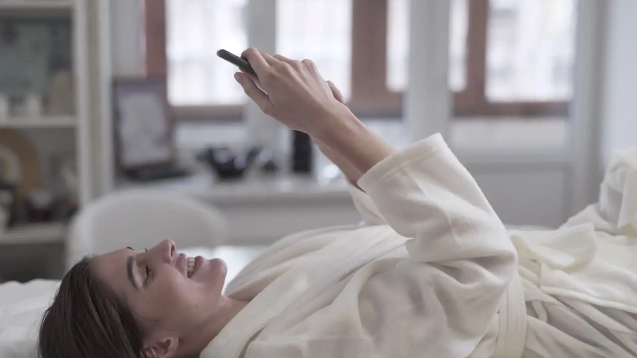 Woman smiling and texting on her phone while laying on the table at a spa