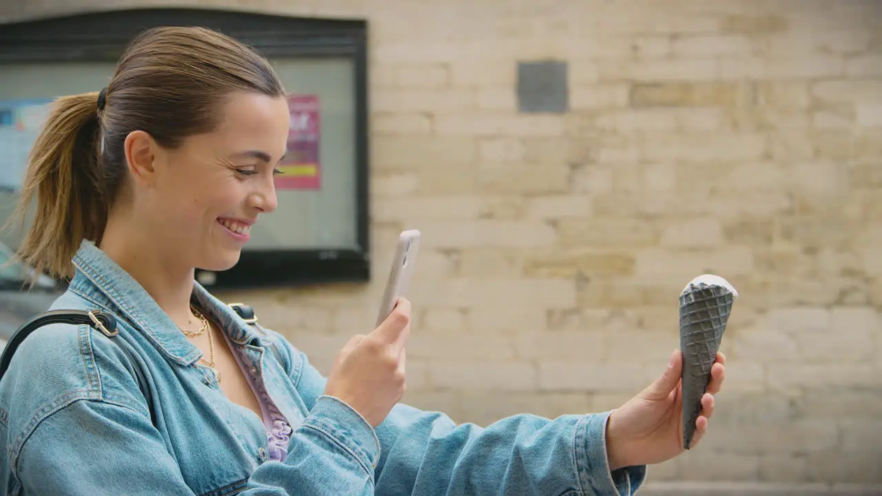 Young Woman Taking Photo Of Ice Cream Cone With Mobile Phone To Post On Social Media