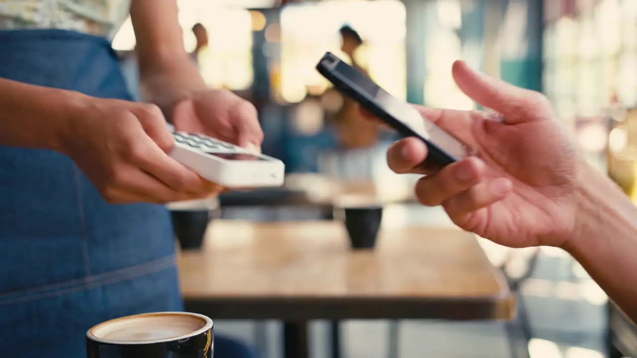 Close Up Of Man In Coffee Shop Paying Bill With Contactless Mobile Phone Payment