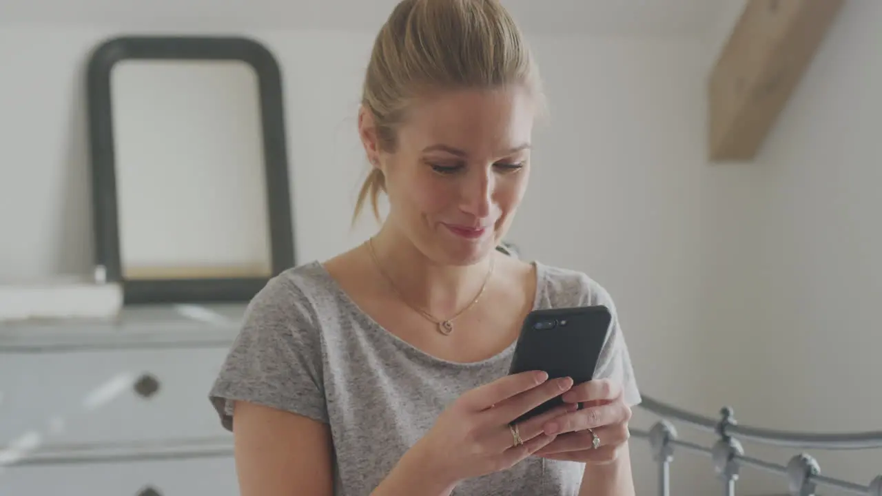 Smiling Young Woman Sitting On Bed With Mobile Phone Wearing Pyjamas