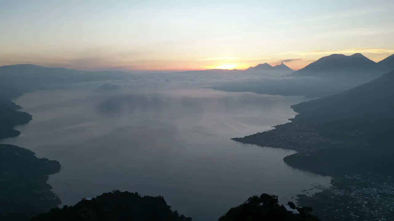 Drone view in Guatemala flying back from a blue lake surrounded by green mountains and volcanos on a cloudy day in Atitlan