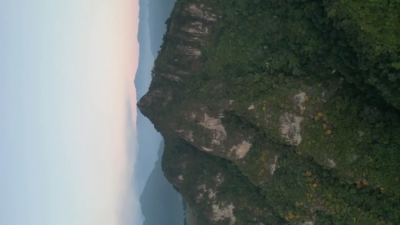 Drone portrait view in Guatemala flying in front of a green mountain surrounded by volcanos on a cloudy day in Atitlan