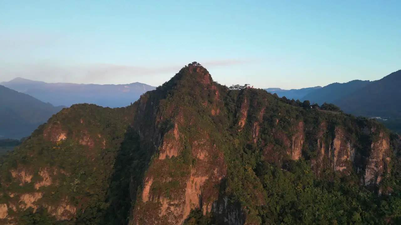 Drone view in Guatemala flying in front of a green mountain face shaped surrounded by volcanos at sunrise in Atitlan