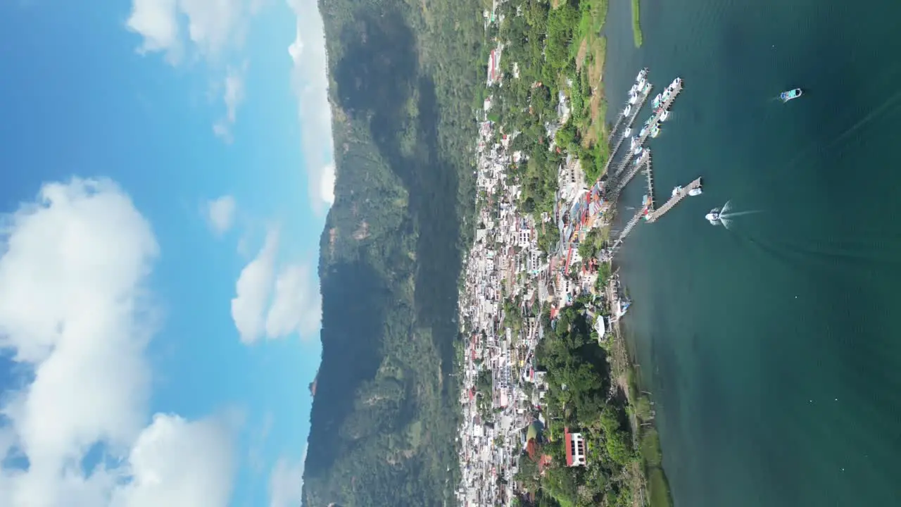 Drone portrait view in Guatemala flying over a blue lake surrounded by green mountains and volcanos on a sunny day in Atitlan