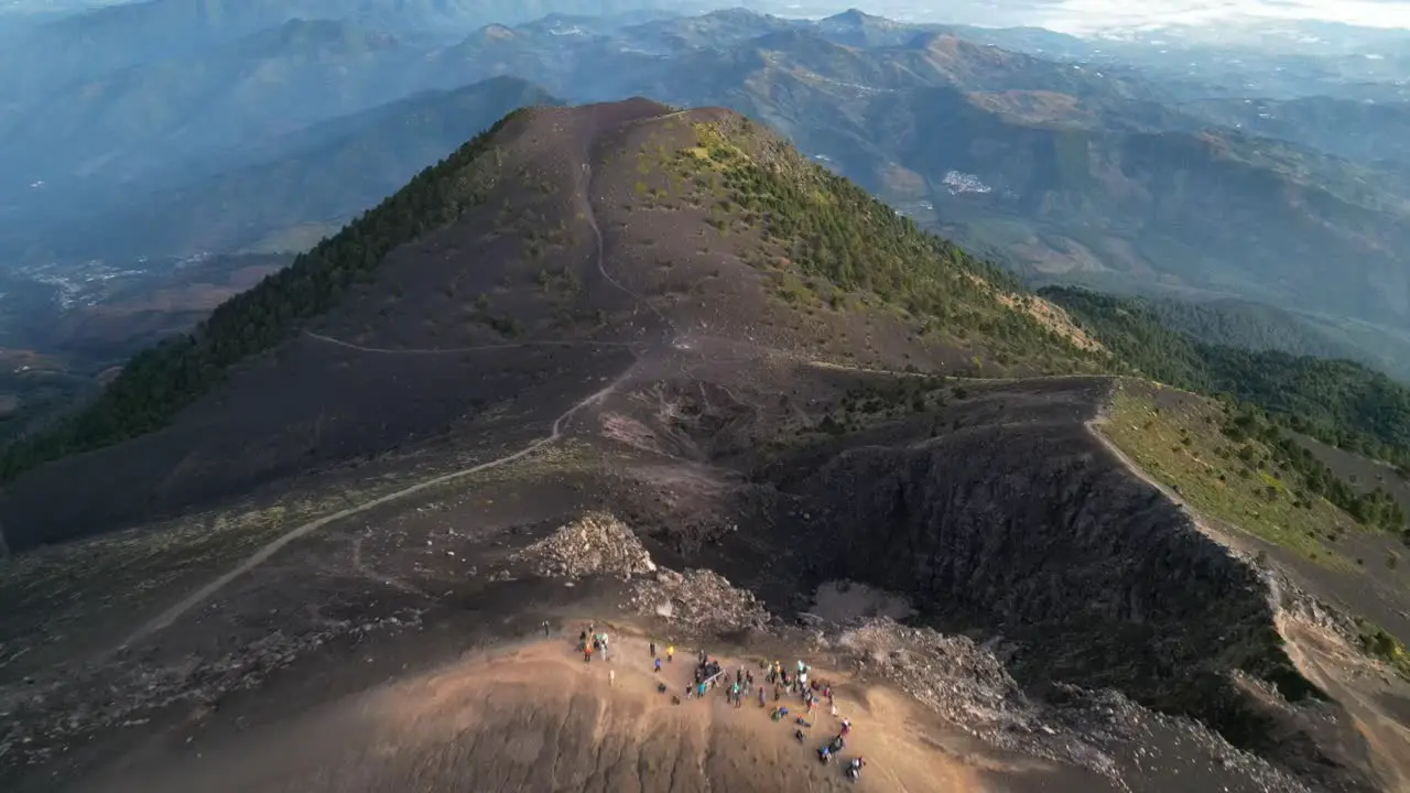 Drone view in Guatemala flying back over a volcano crater at sunrise surrounded by green mountains covered in ashes