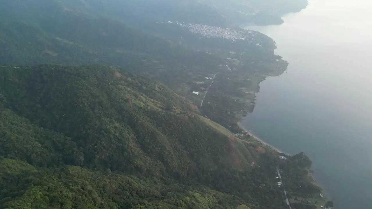 Drone view in Guatemala panning down a green mountain with a forest full of trees and a lake on a cloudy day in Atitlan